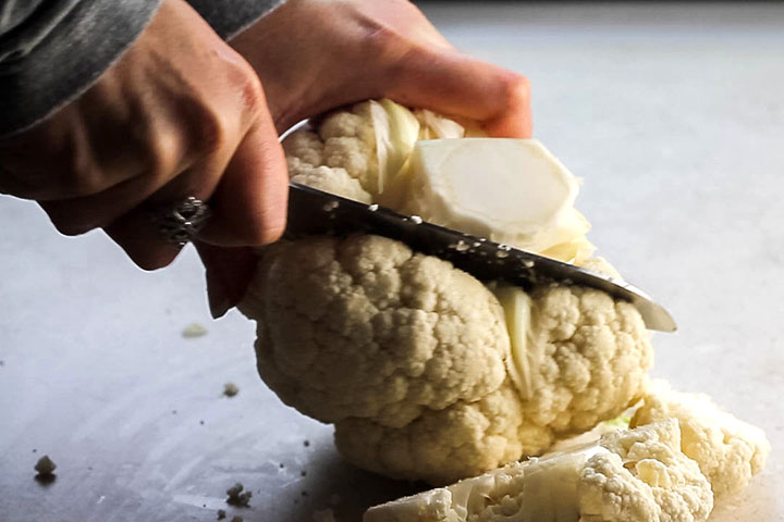 A head of cauliflower being cut on a cutting board.