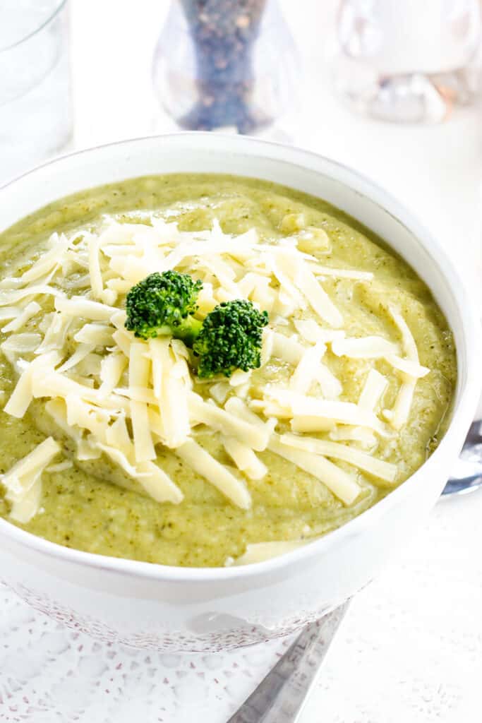 A bowl full of Healthy creamy broccoli soup with shredded cheese and broccoli on top.