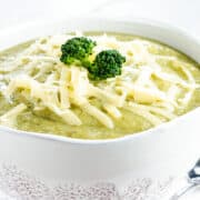 An image showing a white bowl filled with broccoli soup, garnished with shredded cheese, up close.