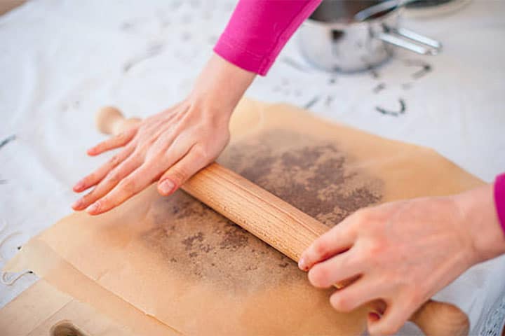 Cookie dough being rolled between two sheets of baking paper