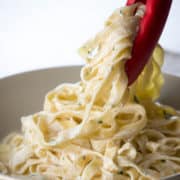 Fettuccine Alfredo being served into a bowl with tongs