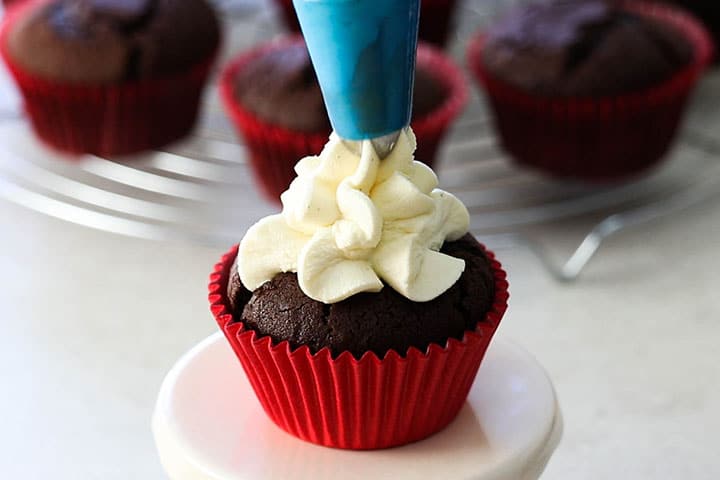 Whipped cream frosting being piped into a chocolate cupcake.