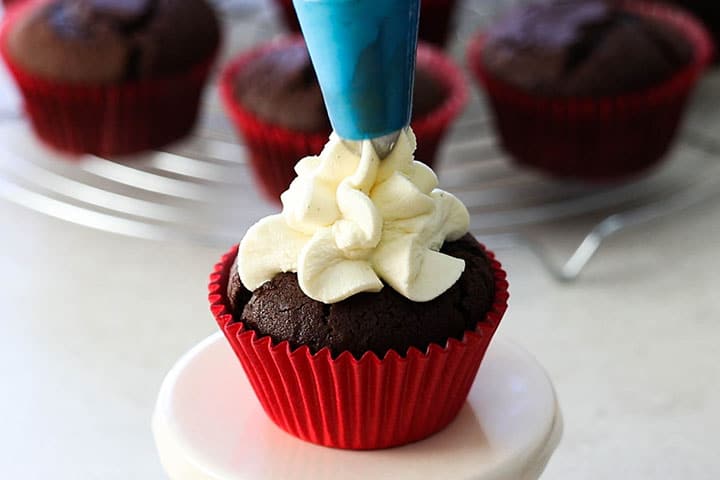 Whipped cream frosting being piped into a chocolate cupcake.