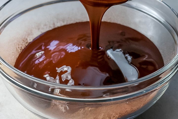 The chocolate mixture being poured into the bowl with the dry ingredients