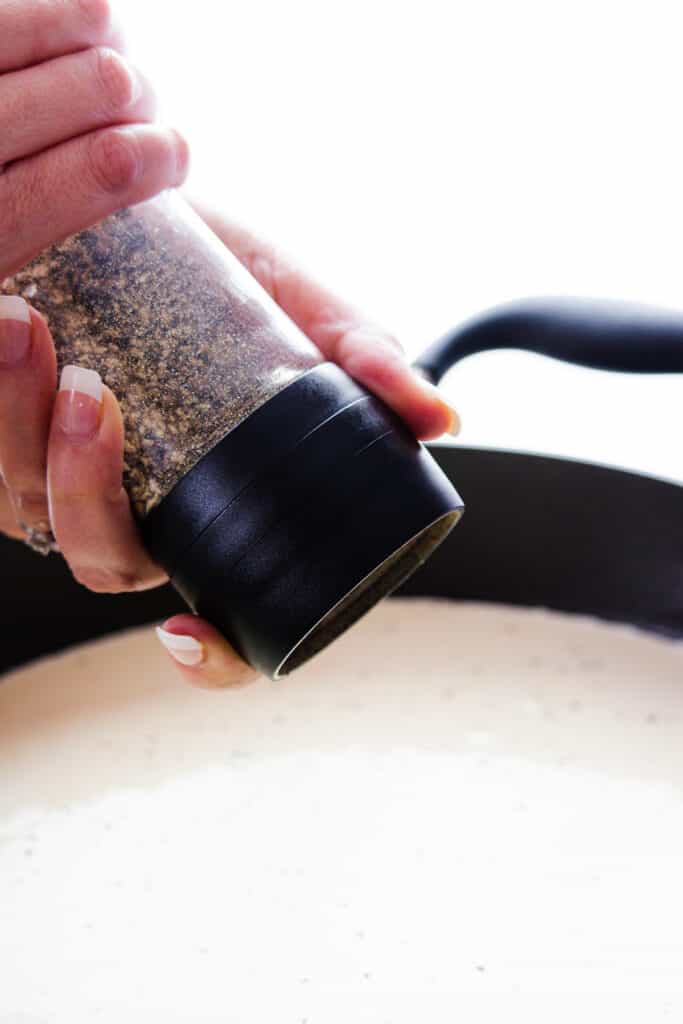 pepper being grated into the sauce with a peppermill 