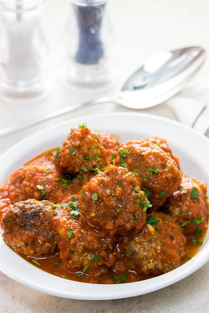 A dish of Meatballs in red sauce sprinkled with fresh parsley.