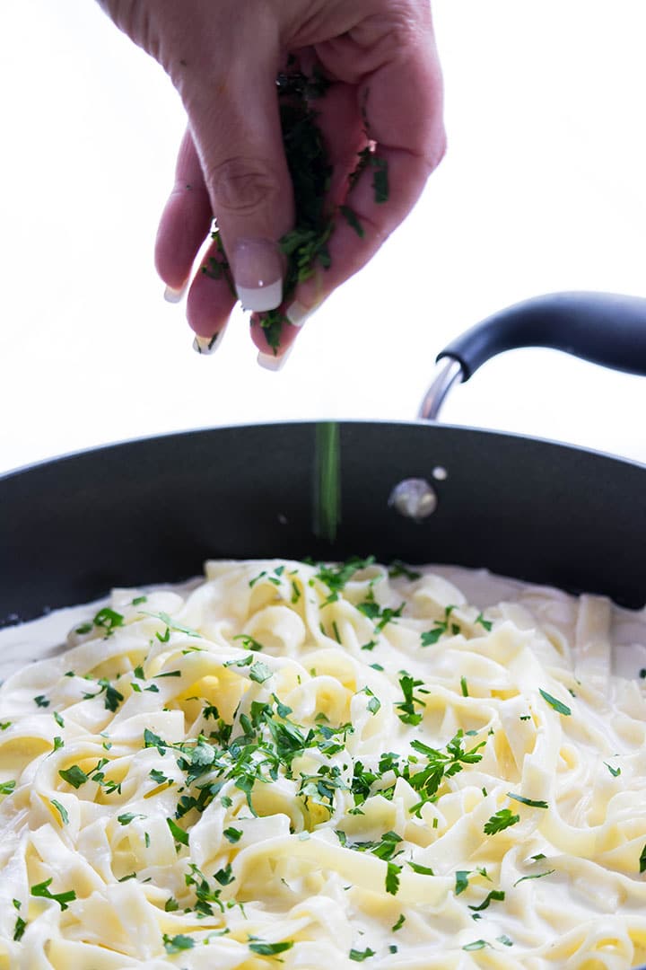 the parsley being added to the Fettuccine Alfredo