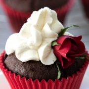 A chocolate cupcake with a red casing, whipped cream icing and a small red rose for decoration