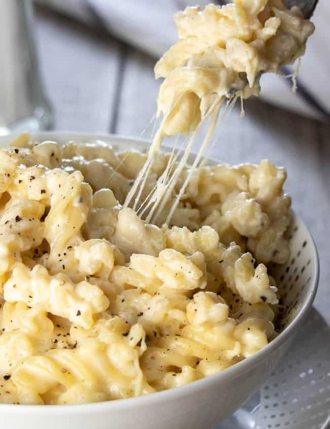 A fork digging into a big bowl of Homemade Creamy Mac and Cheese with cheese stretching from the dish