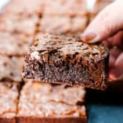 a woman's hand holding a fudgy brownie over a tray of Chocolate Chip Brownies