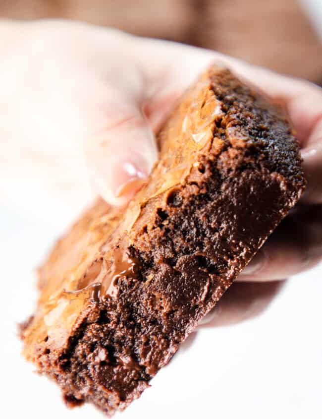 a close up image of a woman's hand holding a fudgy Chocolate Chip Chip Brownie