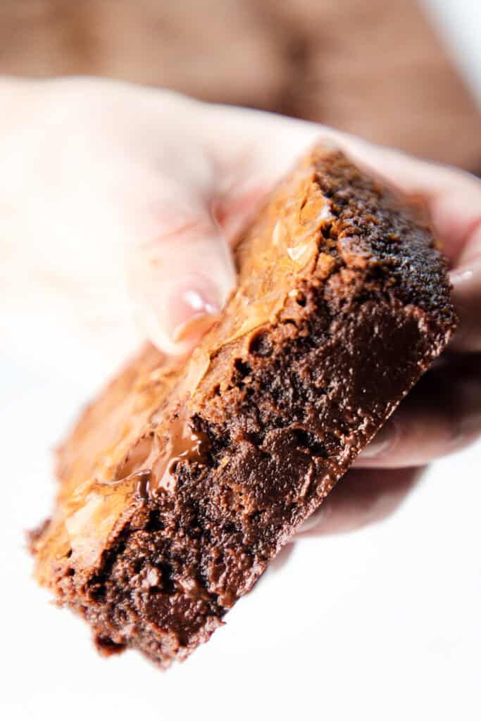 a close up image of a woman's hand holding a fudgy Chocolate Chip Chip Brownie