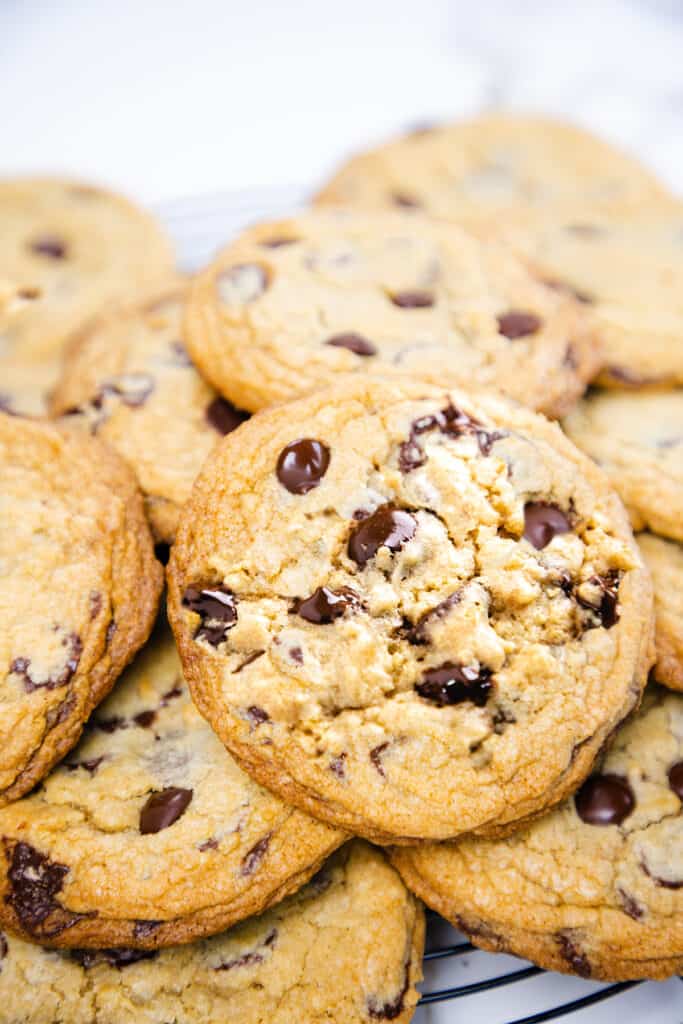 Freshly baked chocolate chip cookies piled on a cooling rack