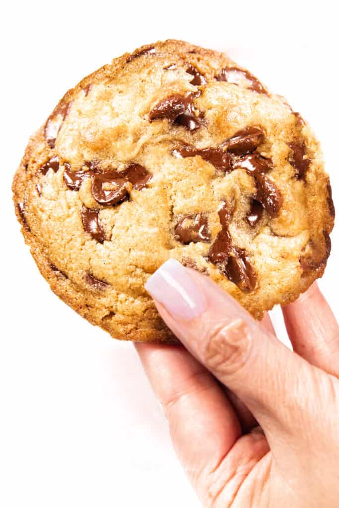 a hand holding a Perfect Chocolate Chip Cookie with melted chocolate chips on the surface