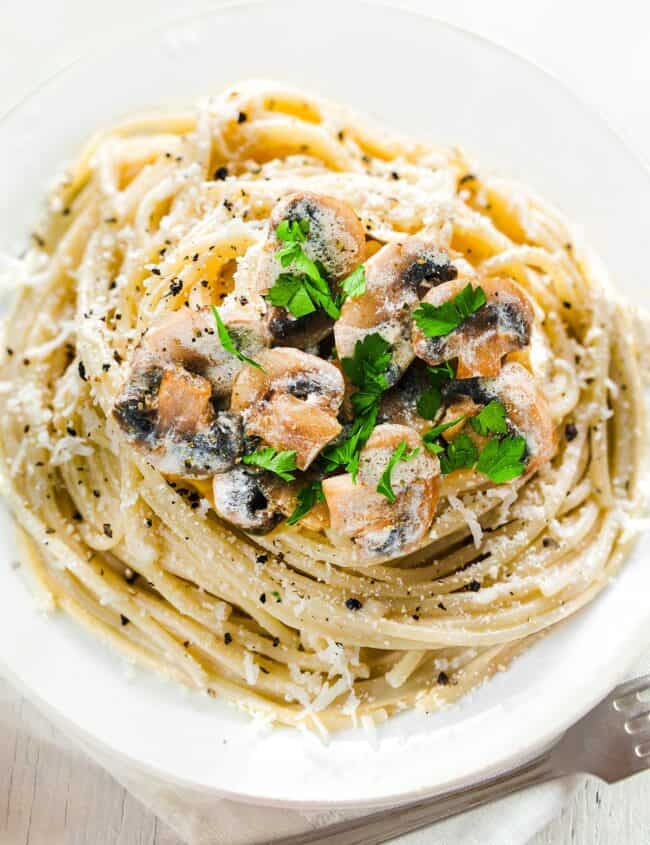a plate of piled high with Creamy Mushroom Spaghetti topped with mushrooms and chopped herbs