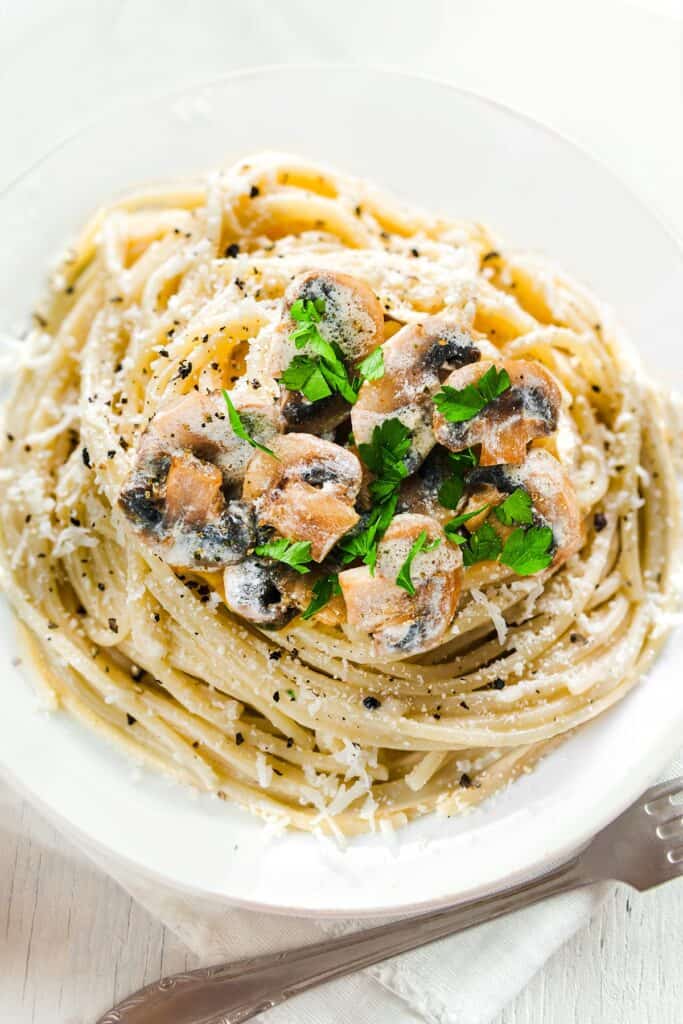a plate of piled high with Creamy Mushroom Spaghetti topped with mushrooms and chopped herbs