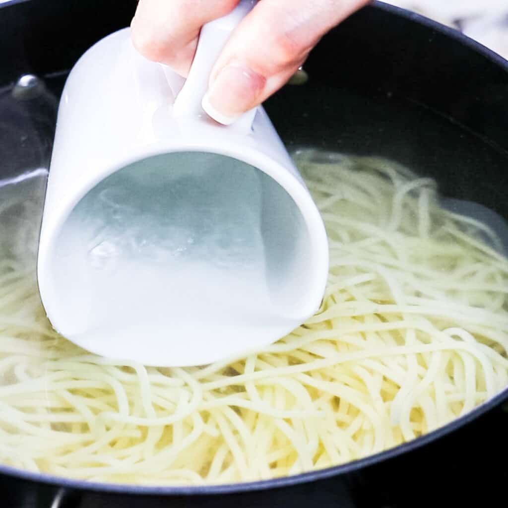 a mug being dipped into the pasta water