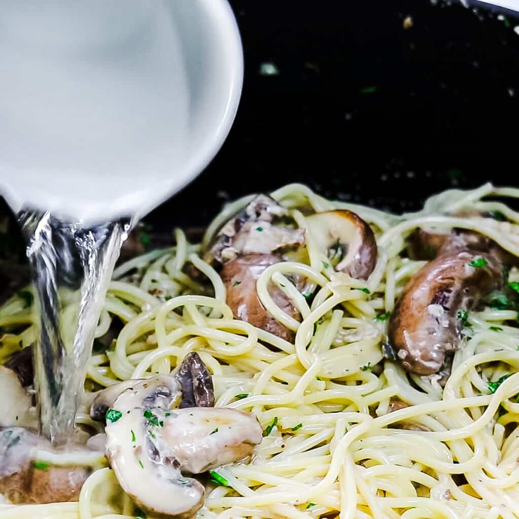 pasta water being poured into the pan with the Creamy Mushroom Spaghetti