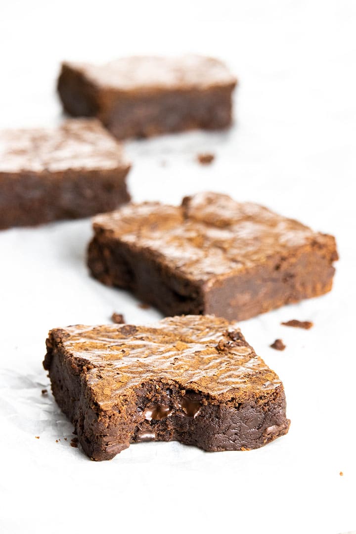 Easy Chocolate Brownies scattered on baking paper with the front one bitten