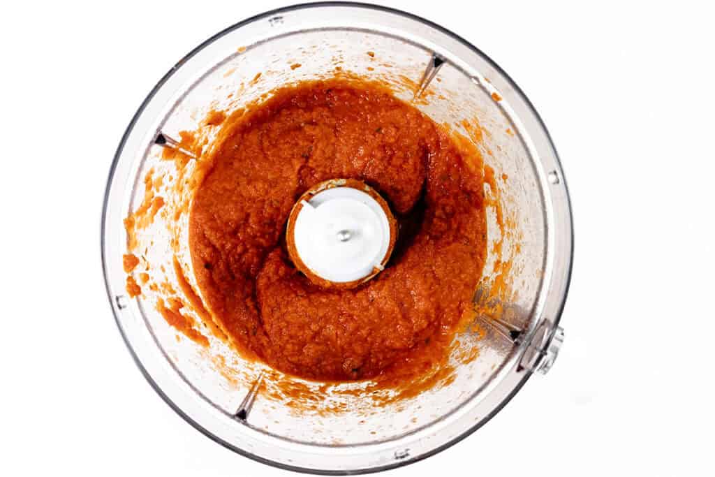 A top-down view of a food processor bowl filled with blended Tomato Sauce, likely tomato-based, against a white background.