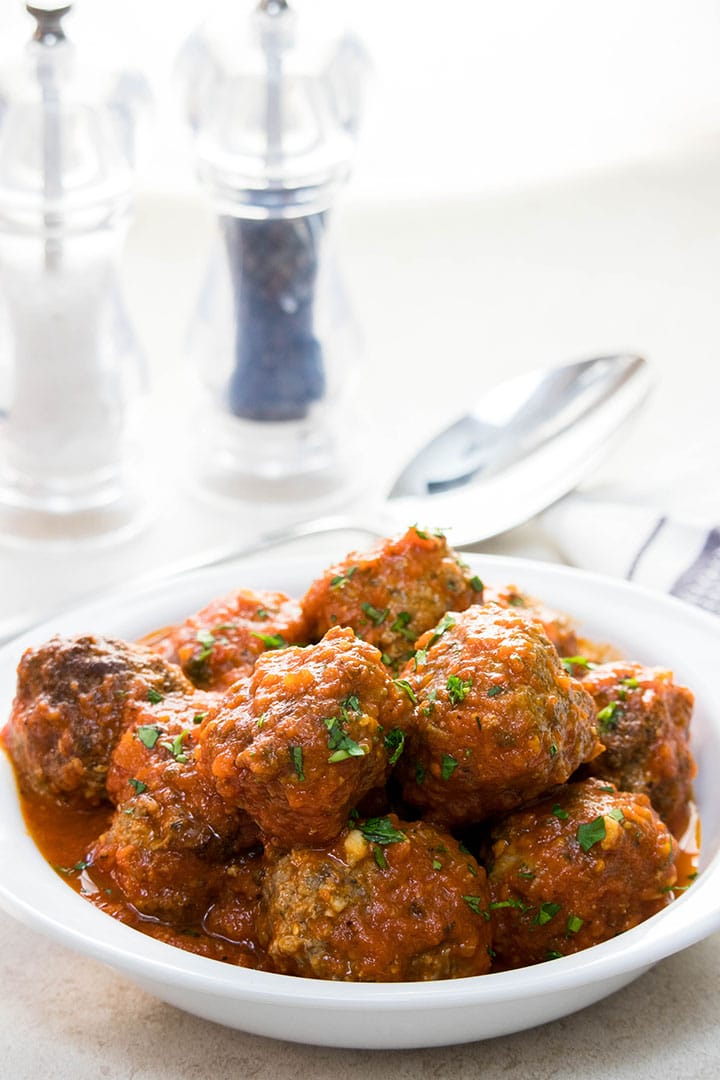 A serving dish full of meatballs with tomato sauce sprinkled with fresh parsley.