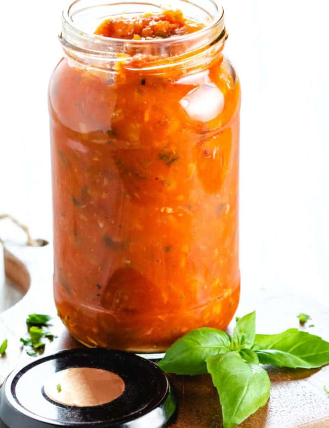 A jar of Tomato Sauce with basil and chopped parsley scattered around it