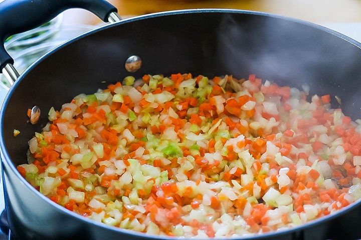 A close up of the carrots, celery and onions sauteing in a pan.