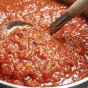 A close up of the tomato sauce being spooned out of a large pot