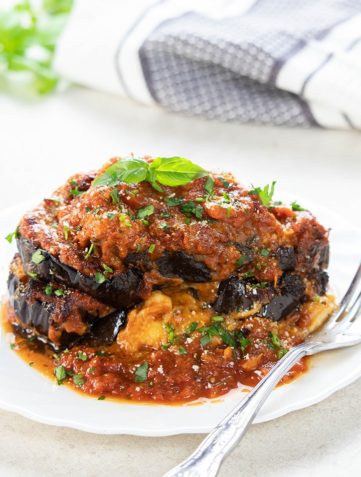 Baked Eggplant Parmesan on a white plate topped with fresh basil