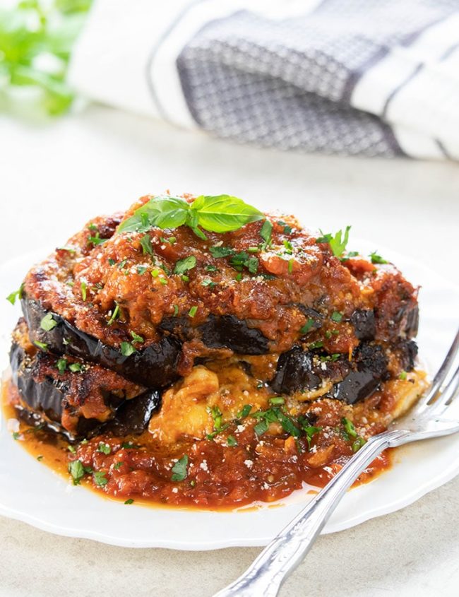 Baked Eggplant Parmesan on a white plate topped with fresh basil