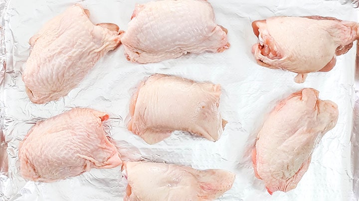 Raw chicken thighs on a baking sheet lined with foil