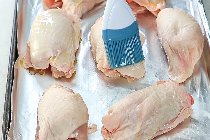 Chicken thighs being brushed with olive oil