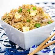 A close up of a bowl of fried rice with chop sticks next to it