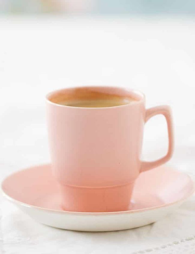 Espresso coffee in pink retro cup and saucer on a lacy white tablecloth against a fresh and floral background.