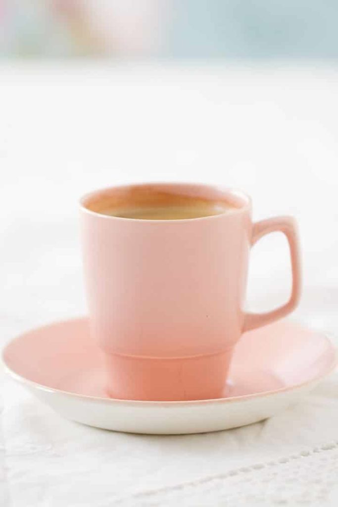 Espresso coffee in pink retro cup and saucer on a lacy white tablecloth against a fresh and floral background.