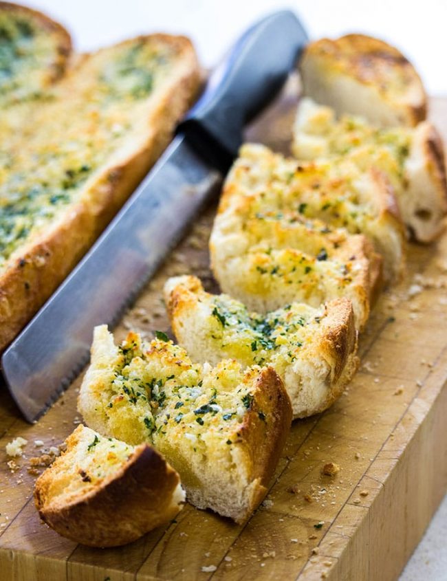 Perfect Garlic Bread sliced on a cutting board with a bread knife next to it