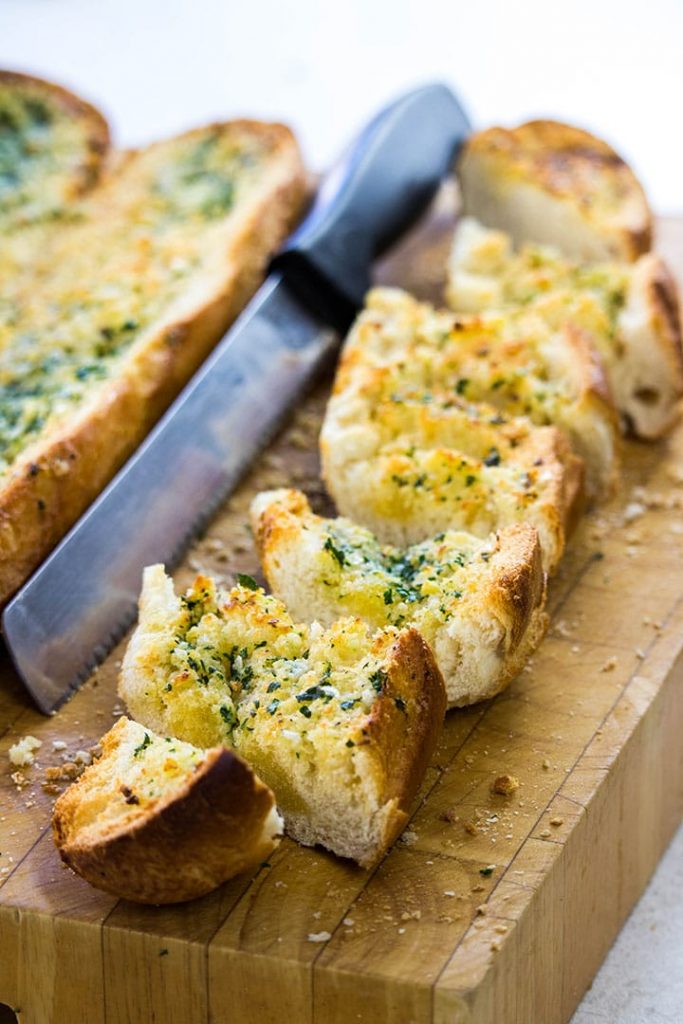 Perfect Garlic Bread sliced on a cutting board with a bread knife next to it