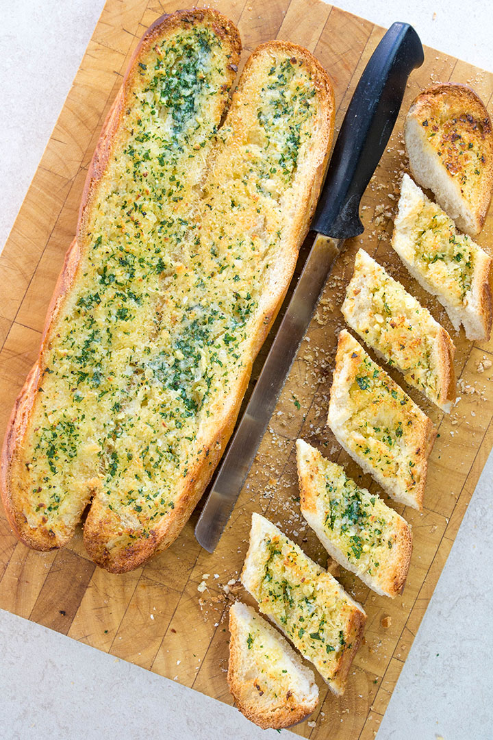 Bread sliced on a cutting board with a 2nd loaf and a bread knife next to it