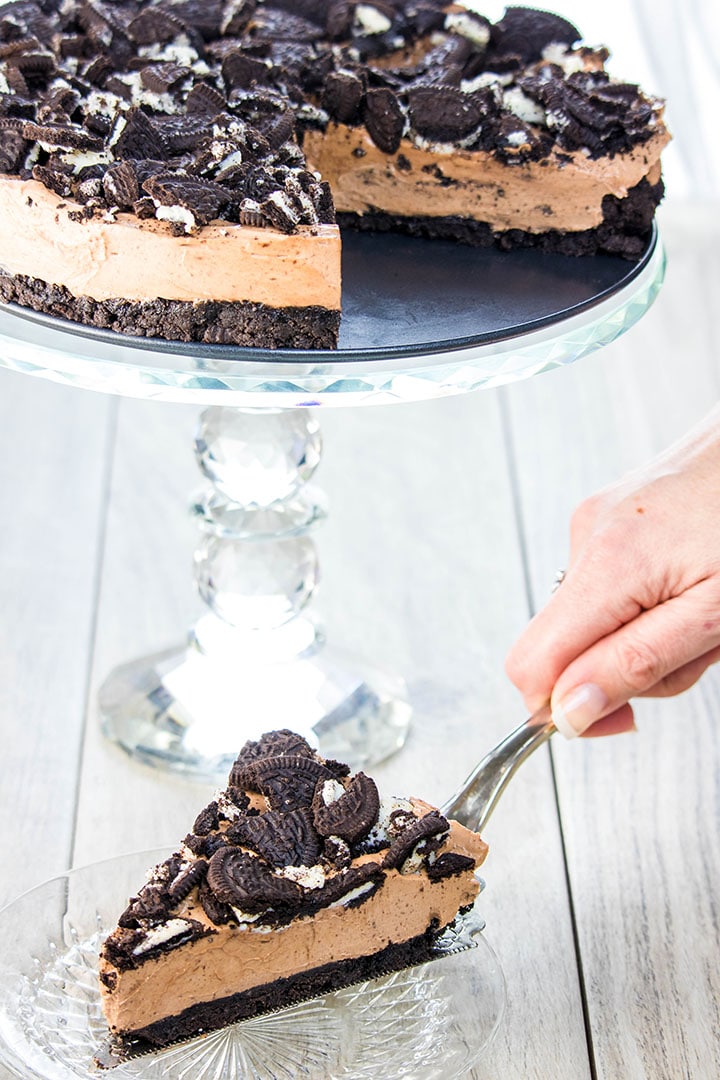 A slice of no bake Oreo cheesecake being served with the cake in the background