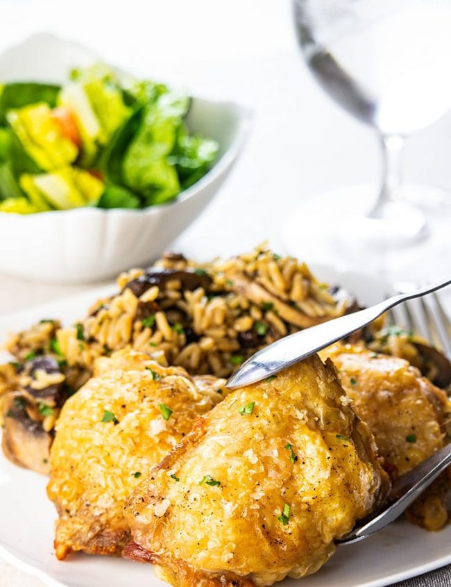 Crispy Oven Baked Chicken Thighs being served on a plate with rice and salad in the background