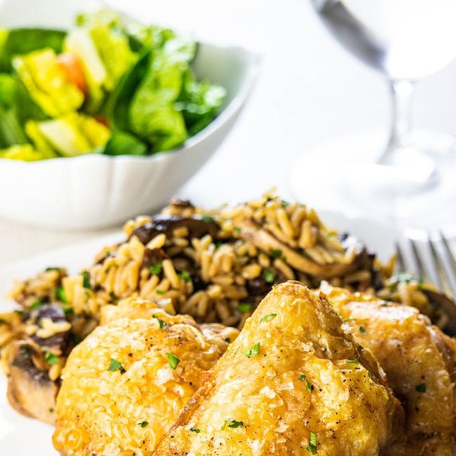 Crispy Oven Baked Chicken Thighs on a white plate with rice and salad in the background