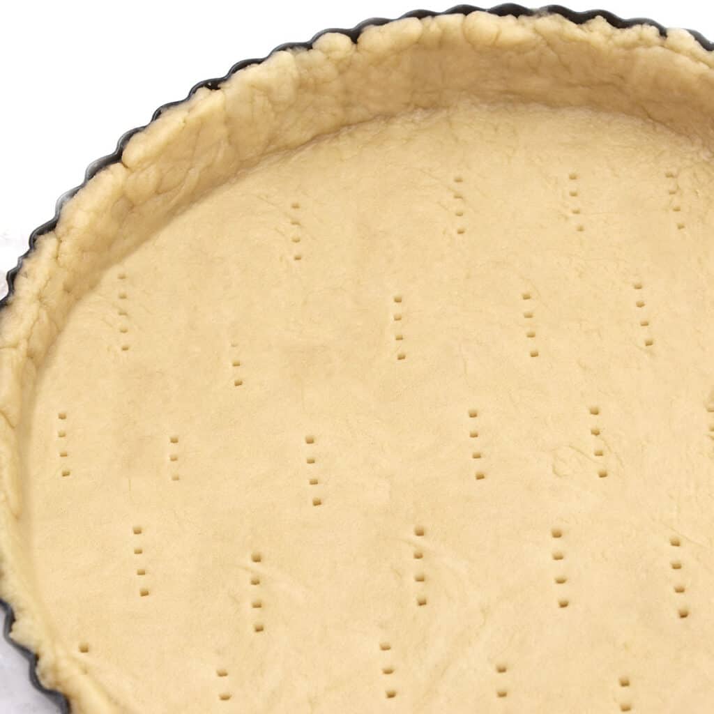 holes in a raw pastry case in a metal baking tin