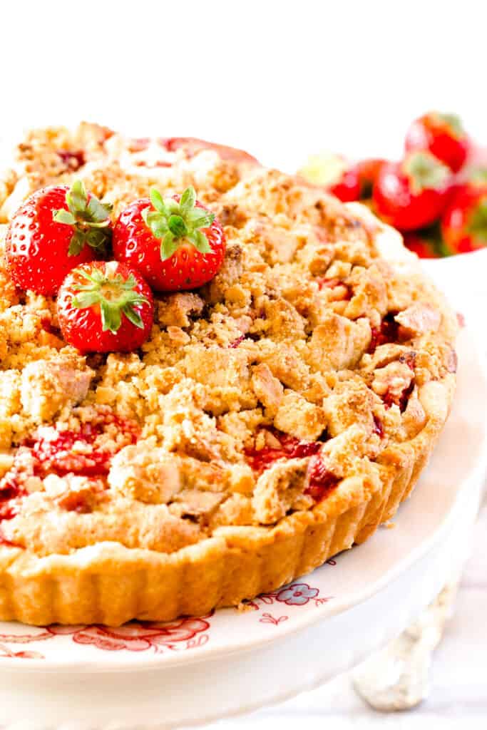 A Strawberry Rhubarb Pie with a crumb topping on a serving plate topped with strawberries.
