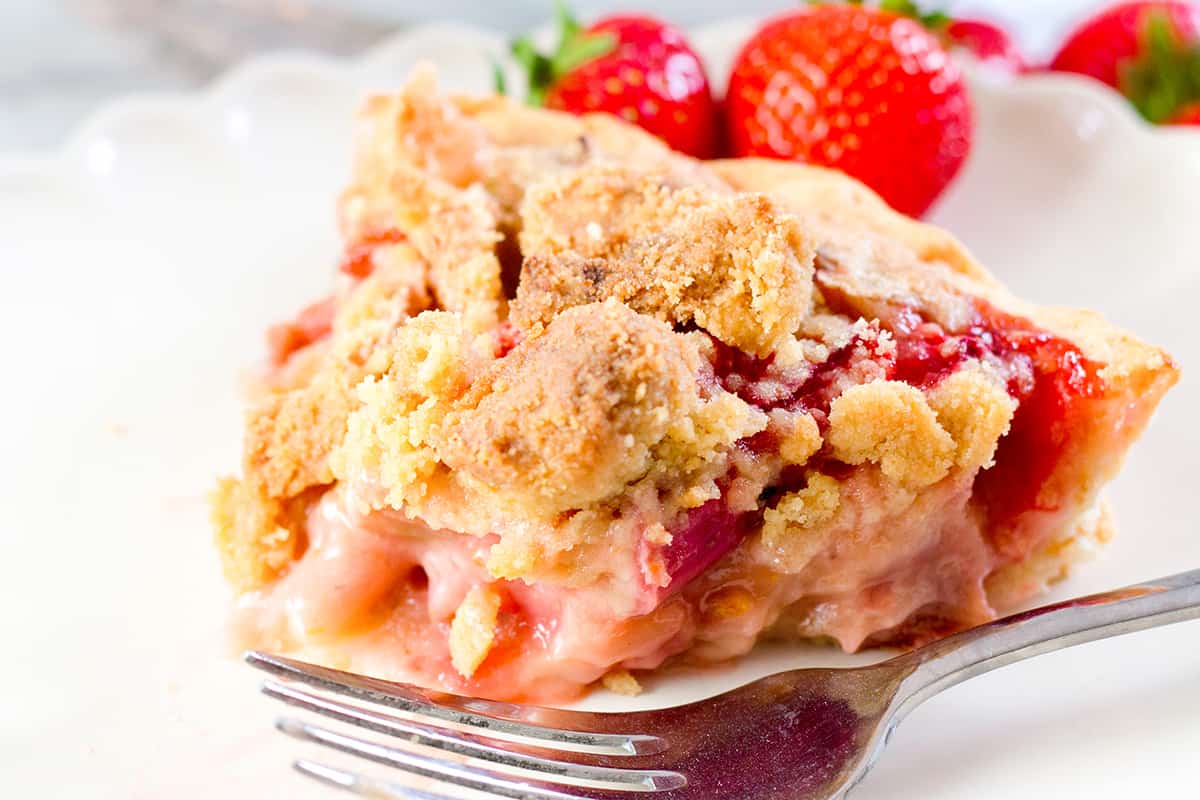 a slice of Strawberry Rhubarb Pie with a fork and stawberries on the plate