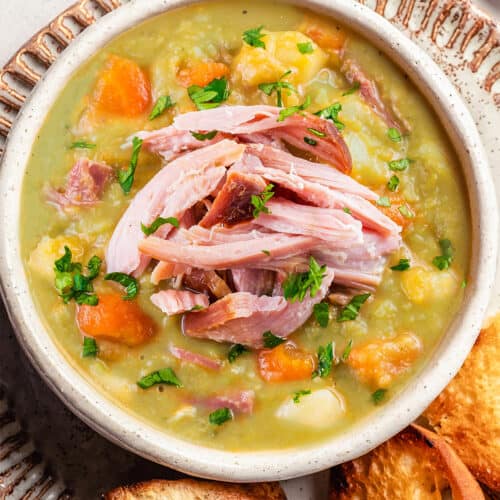 a bowl of split pea soup topped with ham meat with toasted bread on the side