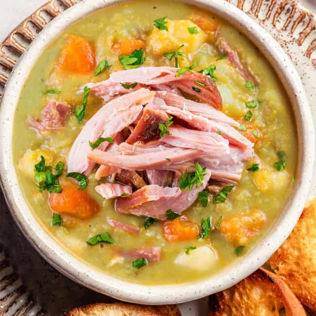 a bowl of split pea soup topped with ham meat with toasted bread on the side