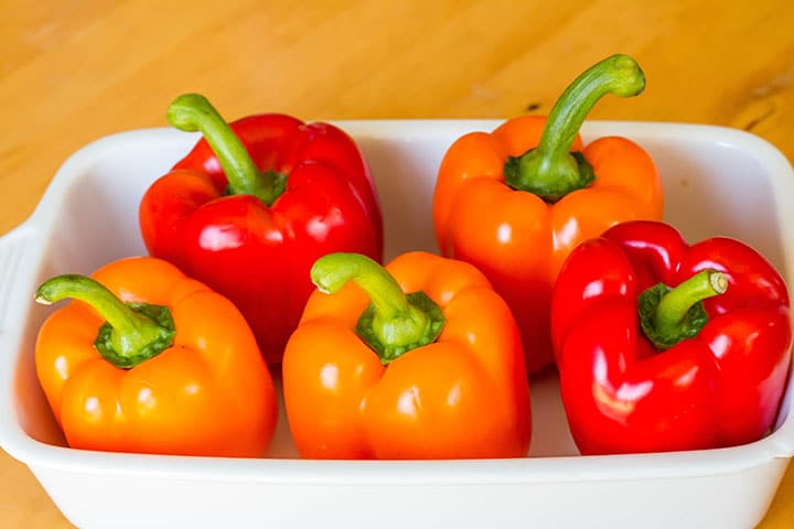 a roasting pan with red and orange peppers placed close together