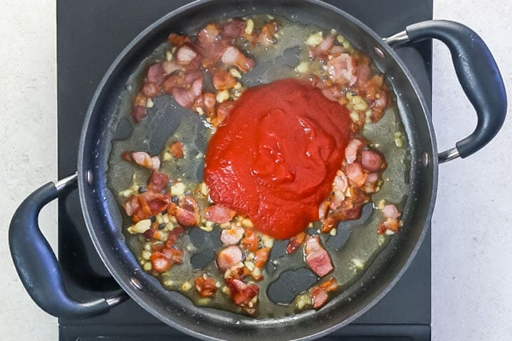 The tomato puree added to the bacon and garlic mixture in the pan