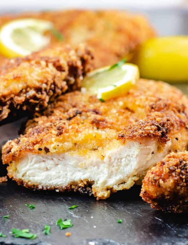 Crispy Breaded Chicken Cutlets on a dish with a piece cut off showing the juicy meat