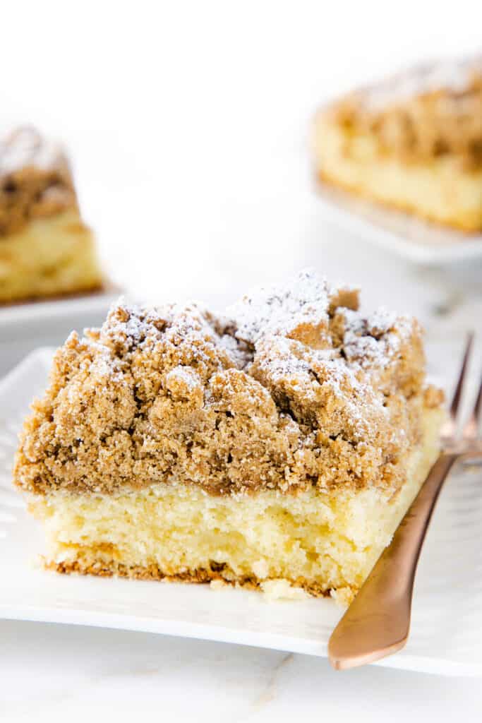 a square of Crumb Coffee Cake on a plate with more slices behind it
